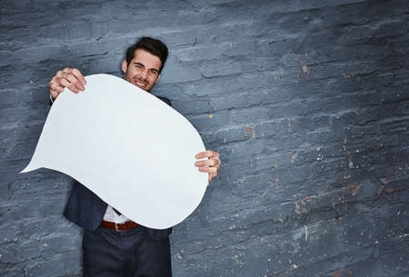 Heres what I have to say.... Shot of a businessman holding a speech bubble against a grey wall.の写真素材