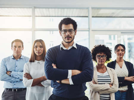 The are very confident in their field of work. Portrait of a group of confident young businesspeople standing with their arms folded inside of the office together.の写真素材