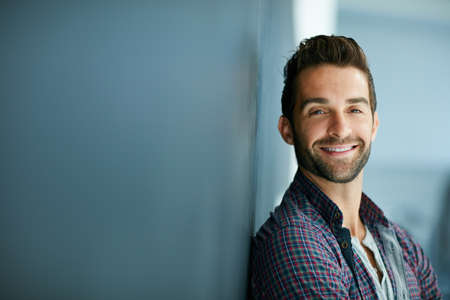 My smile can sell anything. Portrait of a confident young man leaning against a blackboard.の写真素材