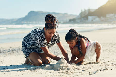 Its their favourite beach activity. Shot of a mother and her little daughter building a sandcastle...