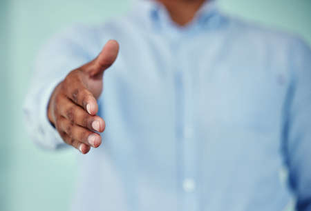 Welcome. Cropped shot of an unrecognizable businessman standing with his hand outstretched for a handshake against a blue background.の写真素材
