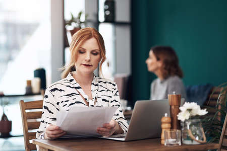 Everything looks in order. Cropped shot of an attractive middle aged woman doing paperwork while being seated inside of a coffee shop during the day.の写真素材