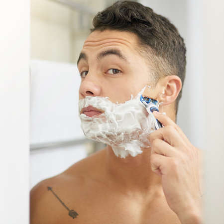 Keeping a clean face. Cropped shot of a young man shaving his beard.の写真素材