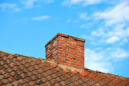 Red brick chimney designed on slate roof of a house building outside with cloudy blue sky background and copyspace. Construction of exterior escape chute built on rooftop for fireplace smoke and heatの写真素材