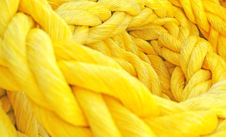 Strong thick braided colorful rope woven and twined. Yellow thick rope macro closeup laying in a heap. Long twisted strong material symbolizes unity, togetherness, and teamworkの写真素材