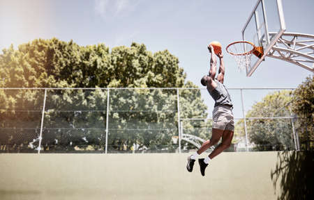 Full length of basketball player dunking a ball into the net during a match on a court. Fit and...