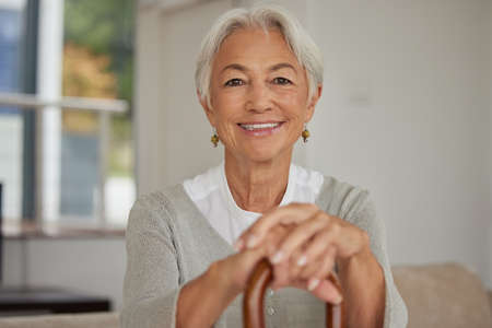 Retired senior woman relaxing at home. Happy smiling old woman holding walking cane and looking at...
