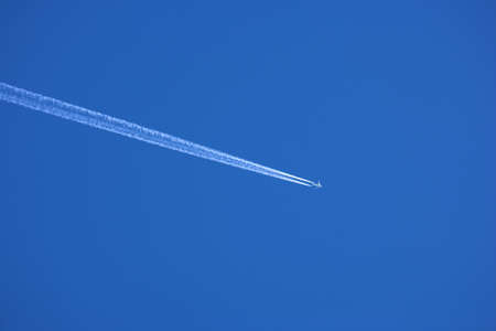 Airplane contrail against clear blue sky background with copyspace. View of a distant passenger jet plane flying on high altitude in blue sky leaving long white smoke trail behind. Air transportationの写真素材