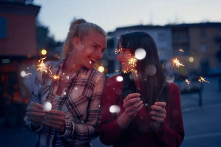 Excited friends celebrating on holiday together playing with sparklers. Happy women on holiday using fireworks to celebrate. Two young women celebrating playing with fireworks on holiday togetherの写真素材