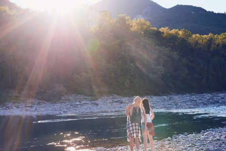 Two women next to a river taking a break during a hike in nature. Two friends hiking in nature enjoying the view and taking a break next to a river. Two women standing by a river enjoying the viewの写真素材