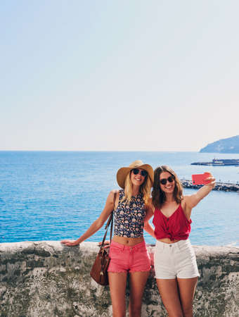 Two friends taking selfies on summer vacation. Girl friends on travel adventure taking photos for social media with smartphoneの写真素材