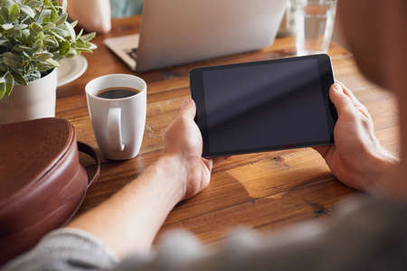 A man using his digital tablet while sitting at his tableの写真素材