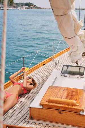 Young woman in a red bikini sunbathing on a boat lying down using her smartphone to send messages....