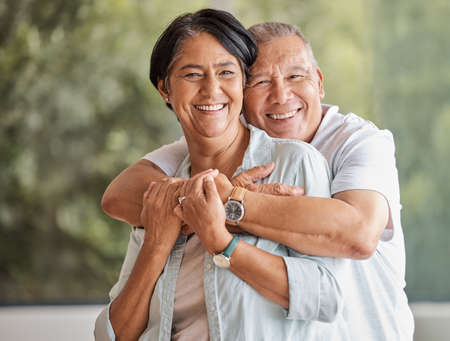 Portrait of a happy senior couple standing in the lounge showing affection by hugging. A loving husband and wife bonding looking at a camera. The man and women are enjoying their time togetherの写真素材