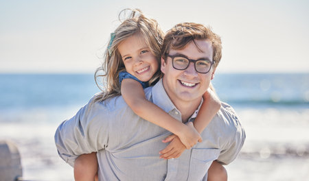 Portrait of happy caucasian father with glasses giving his daughter a piggyback ride on his back at...