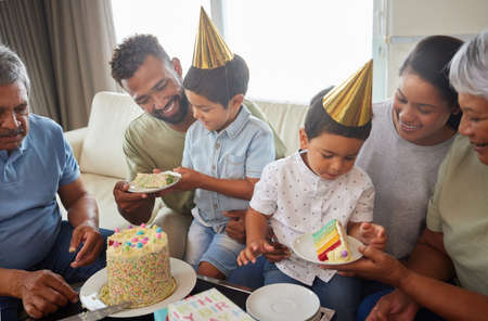 Mixed race family celebrating a birthday and having come cake at home in the loung. Hispanic relatives enjoying some sweet cake and smiling at homeの写真素材