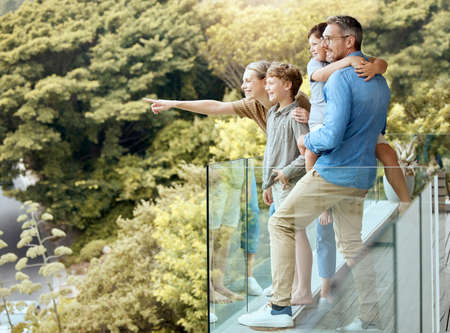 A happy caucasian family of four enjoying the view from a balcony at home. Smiling couple bonding...