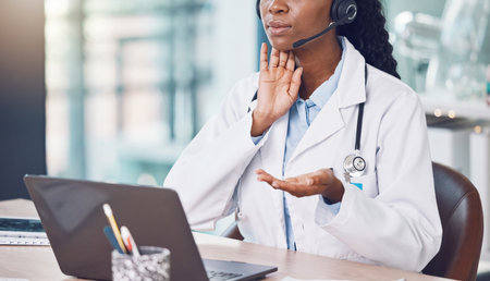 Closeup african american woman doctor using her laptop to do an online remote consult while sitting in her office in the hospital. Testing during the pandemic outbreak. Stop the spread of covid 19の写真素材