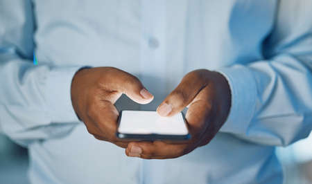 Closeup hands of african man using a phone while standing in his office. African american business...