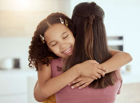 Mixed race single mother and daughter hugging in living room at home. Smiling hispanic girl...