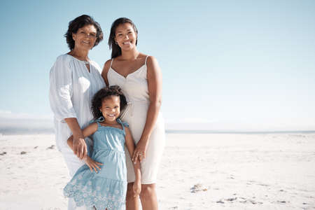 Smiling mixed race family standing together on a beach with copyspace. Happy hispanic grandmother...