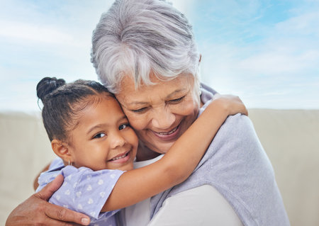 Smiling adorable little mixed race girl hugging her grandmother while bonding with her at home....