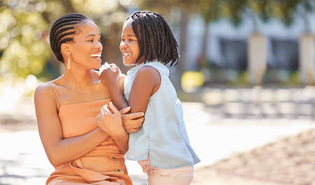 Happy young woman and her daughter spending quality time together outside in the park during summer....