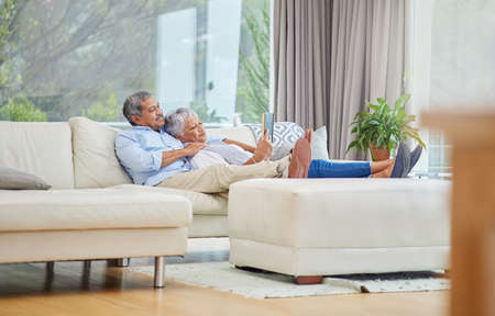 Closeup of an affectionate mixed race senior couple relaxing and reading a book in their living room at home. Hispanic man and wife bonding on the sofa in the living room being affectionateの写真素材