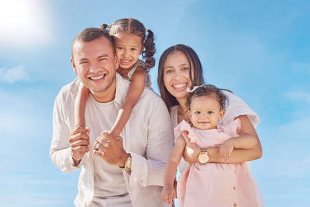 A happy mixed race family of four enjoying fresh air at the beach. Hispanic couple bonding with their daughters while standing and carrying their daughtersの写真素材