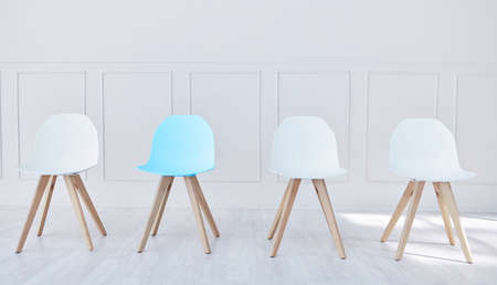 Four chairs lined up in an office waiting room. One blue chair and three white, waiting for potential job candidates to be seated, interviewed and potentially hired by human resources for a new careerの写真素材