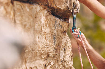 Closeup shot of an unrecognizable man using a carabiner while mountain climbing. Unknown male checking his safety equipment while adjusting his rope and hook and doing extreme sports outside in natureの写真素材