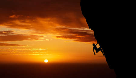 Unrecognizable adrenaline junkie doing extreme sports. Unknown man doing mountain climbing at sunset. Dark shot of a young male passionate about his fitness while doing his favourite hobbyの写真素材
