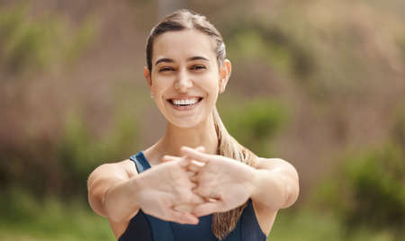 Portrait of one fit young mixed race woman stretching arms for warmup to prevent injury while exercising outdoors. Female athlete preparing body and muscles for training workout or run at the parkの写真素材