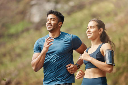 Fit young man and woman running together outdoors. Interracial couple and motivated athletes doing...