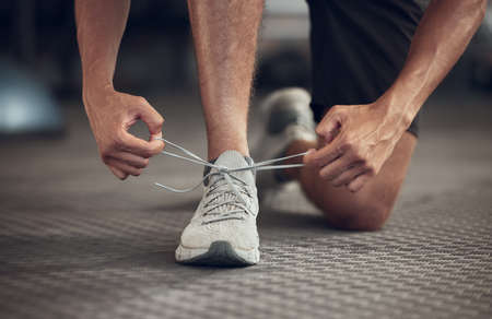 Closeup of athlete tying his shoelaces in the gym. Hands of fit man getting ready with his gym...