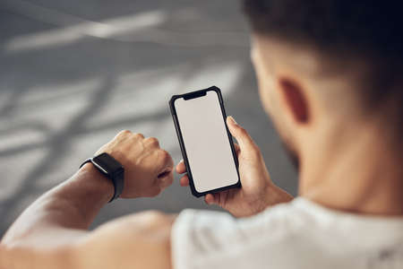 Athlete using their smartphone to track their progress. Fit man using a watch to track workout...