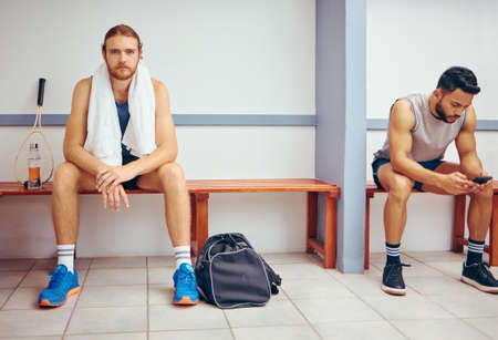 Portrait of a caucasian athlete sitting in a locker room. Two men sitting in a gym locker room...