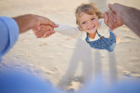 Portrait close up of a girl being lifted by her father while playing at the beach outside during sunset. Caucasian race girl having fun outside on the beachの写真素材