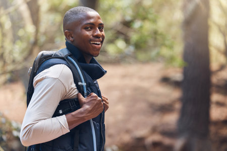 One young handsome african american male backpacker hiking outdoors in the woods. Confident and happy black man walking through the forest, sightseeing and enjoying his favourite weekend activityの写真素材