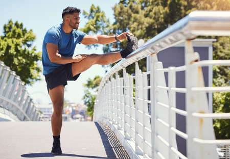 Fit athletic mixed race man stretching on a bridge in the city during his workout. Young hispanic...