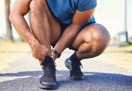 Closeup of active mixed race man holding his ankle in pain while out for a run. Unknown athlete...