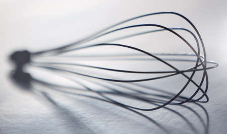 Blurred closeup of stainless steel balloon whisk on a grey table in a modern kitchen. Metallic,...