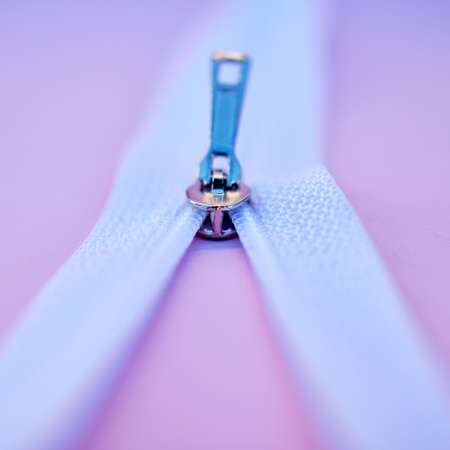 Closeup of a metal zip isolated on a pink background. Macro view of a zipper closing or being unzipped on fabric in a fashion, tailor, or seamstress studio. Clothing design and connection still lifeの写真素材