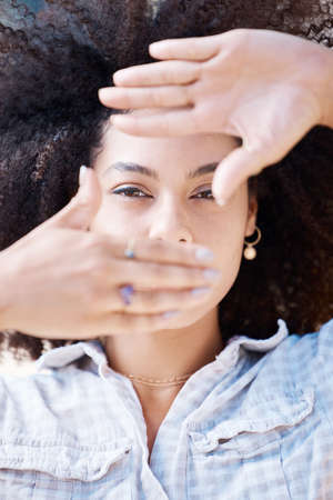 Closeup of a beautiful young mixed race woman with an afro framing her face with her hands. Looking...