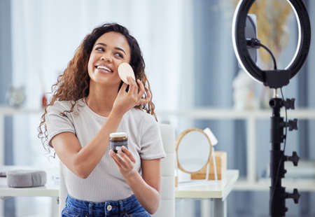 One hispanic woman recording a makeup tutorial for her beauty blog with her phone while sitting at...