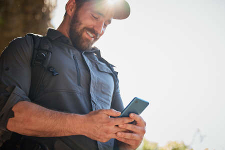 Happy caucasian man using smartphone while carrying a backpack and hiking alone in the mountains on...