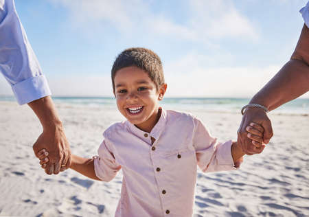 Adorable little boy smiling while walking on the beach with his grandparents and holding hands. Cute mixed race boy enjoying family time at the beachの写真素材