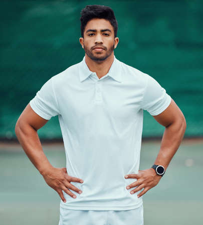 Portrait of serious indian tennis player standing alone on a court. Fit ethnic sports professional with hands on hips and feeling confident in a sports club. Ready for an athletic and healthy gameの写真素材