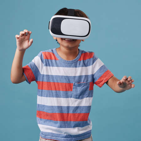 Young mixed race boy standing and wearing a wireless vr headset and playing a video game against a...