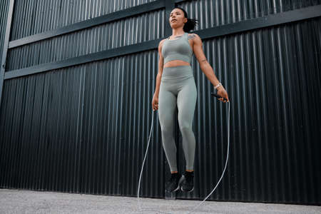 One young african american female athlete skipping using jump rope while exercising outside in the city. Beautiful and dedicated mixed race sportswoman working out alone against an urban backgroundの写真素材